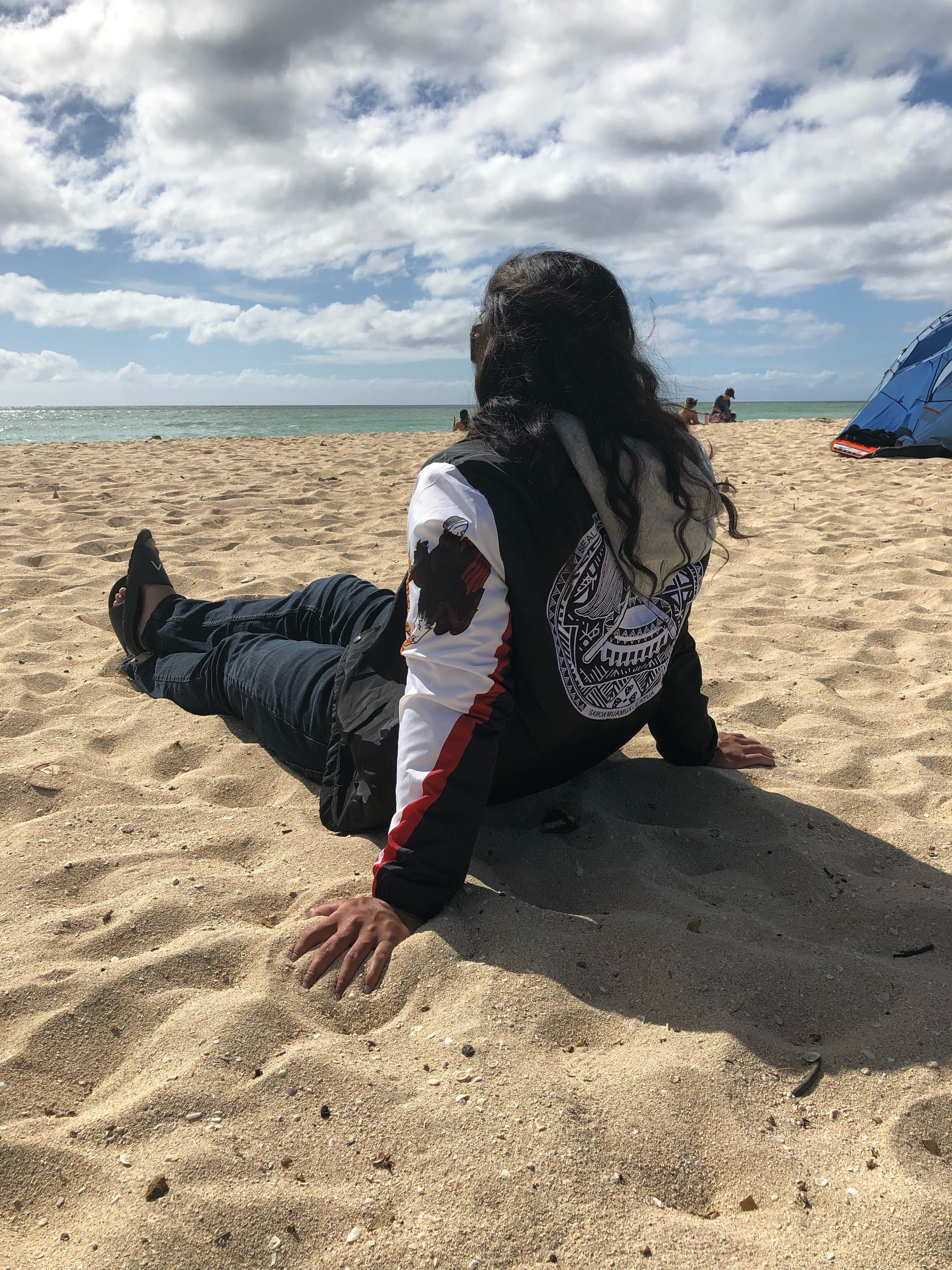 A man laying by the beach wearing the Island Dynasty American Samoan Windbreaker